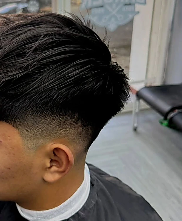 Fade medio con el pelo largo arriba peinado hacia un lado, junto al ventanal del local